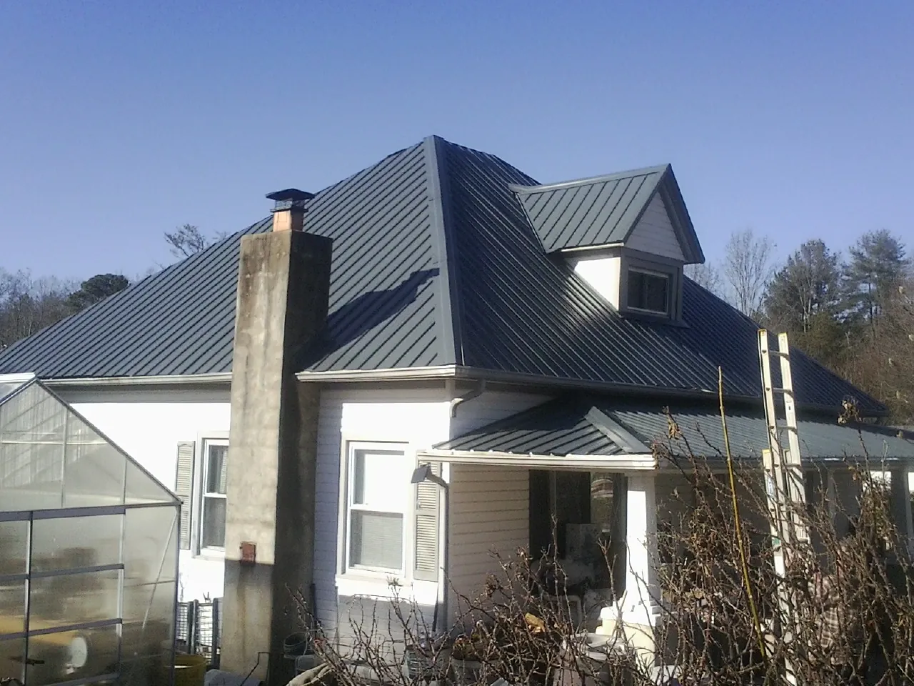 Dark blue standing seam metal roof on a white farmhouse with dormer — Slate & Tile Roof Repair by Roofing Brothers in White Stone