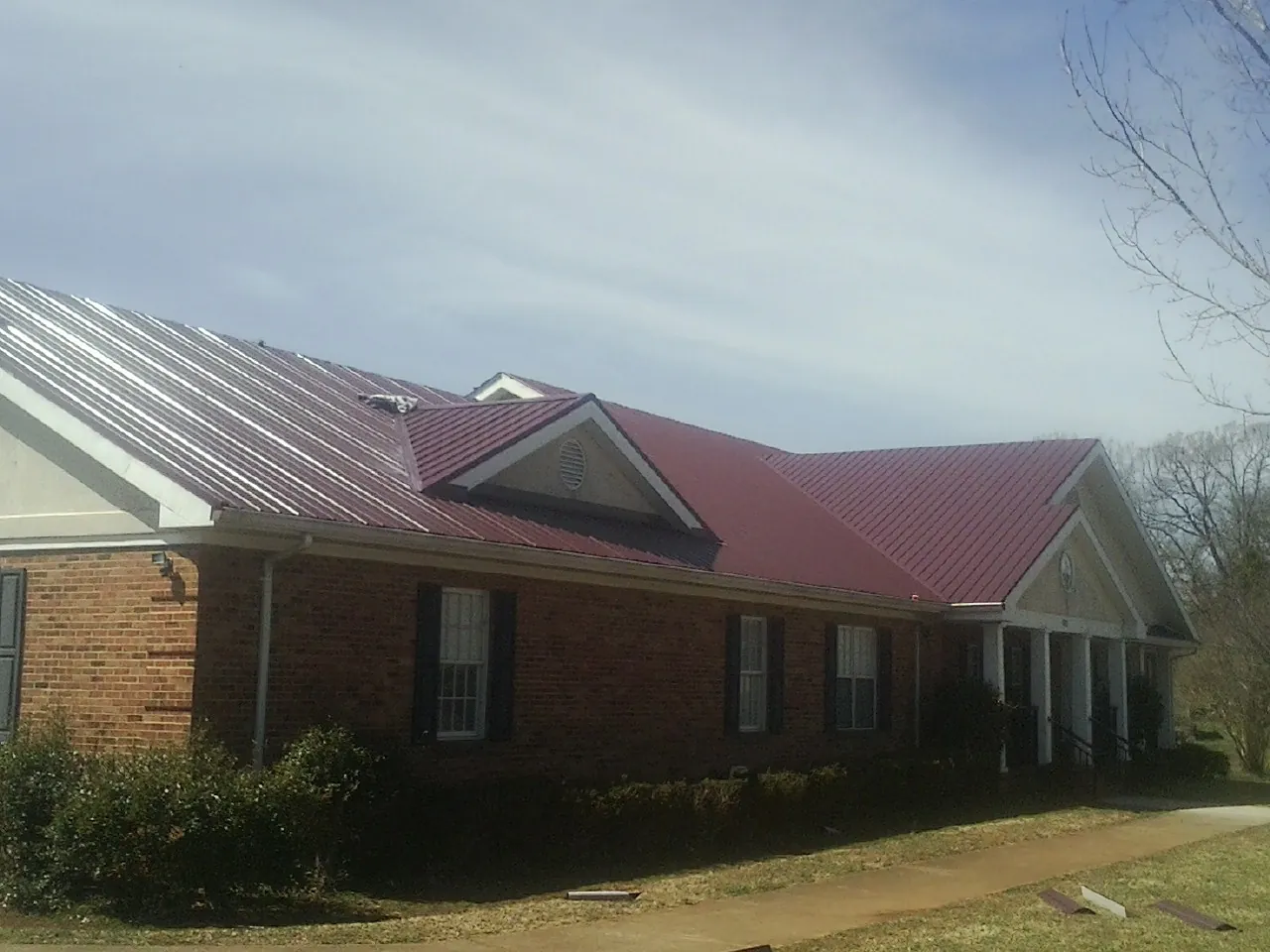 Red metal roof with gabled entries on a long brick building, from a Hail Damage Roof Repair job in White Stone