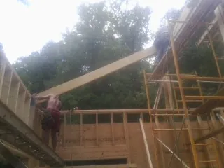 Carpenter raising a rafter beam on a new second story frame in White Stone