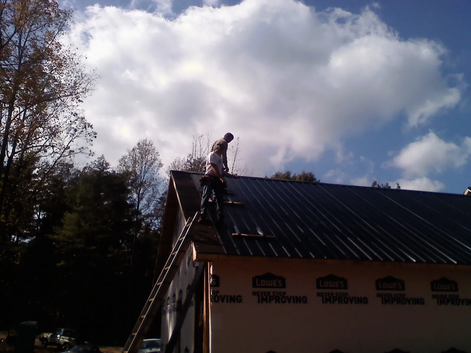 Roofer fastening dark metal panels high against a cloudy sky, from a Roof Inspection job in White Stone