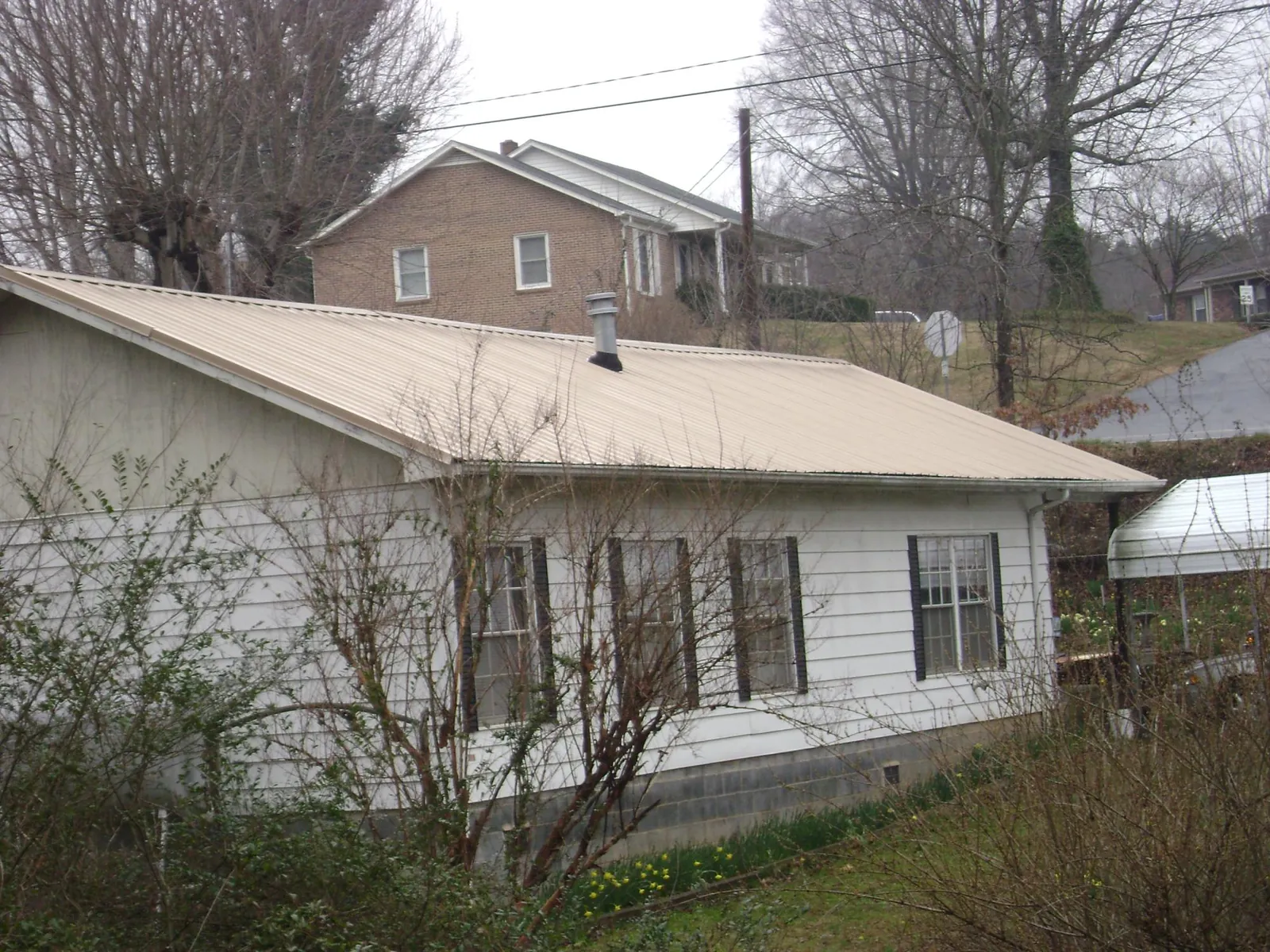 Tan metal roof on a white sided house set into a hillside — Commercial Roofing by Roofing Brothers in White Stone